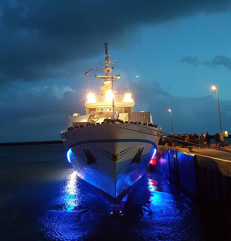 Frontansicht des Seebäderschiffs Helgoland bei Dämmerung, beleuchtet mit blauem Unterwasserlicht am Kai.